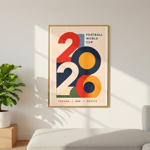 Pu&ograve; includere: Un poster incorniciato con un bordo dorato. Il poster presenta il numero "2020" in forme geometriche audaci e colorate. Il testo in alto recita "FOOTBALL WORLD CUP", e in basso, "CANADA &bull; USA &bull; MEXICO". Lo sfondo &egrave; beige chiaro.