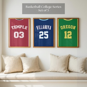 May include: Set of three framed basketball jerseys. The jerseys are red, blue, and green, with the names "Temple", "Villanova", and "Oregon" displayed. Each jersey has a number. The text "Basketball College Series - Set of 3" is above the frames.