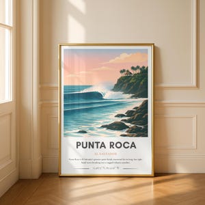 May include: A framed art print featuring a coastal scene with a large wave breaking near a rocky shoreline. The artwork depicts a vibrant sunset with a gradient of pink and orange hues. The text "PUNTA ROCA EL SALVADOR" is displayed at the bottom.