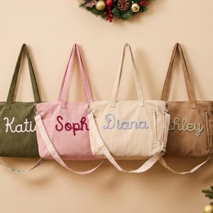 May include: Four corduroy tote bags in olive green, light pink, cream, and tan, each featuring a personalised name embroidered in cursive script. The bags include dual top handles and a detachable, patterned crossbody strap with metal hardware.