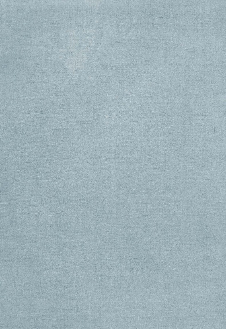 May include: A solid, light blue fabric with a subtle texture. The material has a soft, velvety appearance, and the color is a muted, pastel shade of blue. The fabric appears to be a single piece, suitable for upholstery or apparel.