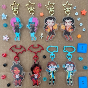 Puede incluir: Colección de llaveros de personajes con cierres de estrella dorada. Los llaveros presentan varios personajes de dibujos animados con diferentes colores de pelo y atuendos. Algunos personajes tienen llamas, otros gafas o cuernos de diablo. También hay cuentas decorativas en forma de estrella y círculo.