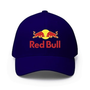 Può includere: Cappellino da baseball blu navy con il logo Red Bull. Il logo presenta due tori rossi uno di fronte all'altro davanti a un cerchio giallo, con la scritta "Red Bull" in rosso sotto.