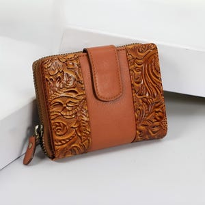 May include: A brown leather wallet with a floral embossed design. The wallet has a zip-around closure and a snap closure. The wallet is made of genuine leather and has a classic, vintage look.