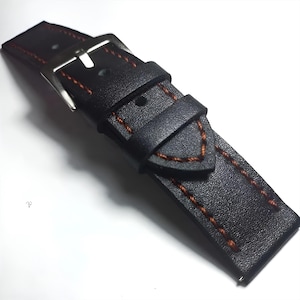 May include: A black leather watch strap with orange stitching. The strap has a silver buckle and a keeper loop. The stitching is visible along the edges and around the keeper. The watch band is designed for a classic look.