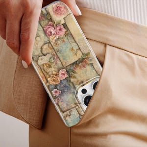 May include: A phone case with a floral design, featuring pink and peach roses on a collage of vintage-style images. The case is partially visible in a tan pocket, highlighting its design and colour scheme.