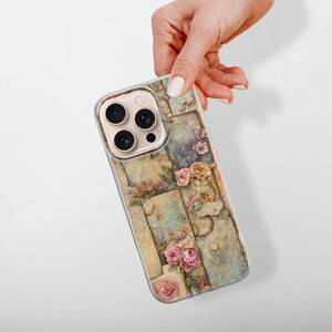 May include: A phone case with a floral design, showing a collage of vintage-style panels with roses and other flowers in pink, yellow, and cream. The case has a gold camera module and a clear border.