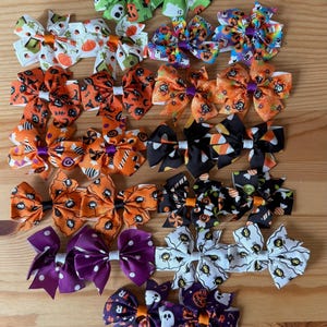 Könnte beinhalten: Eine Sammlung von einundzwanzig Haarschleifen mit verschiedenen Halloween-Motiven, darunter Geister, Kürbisse, Spinnen, Zuckermais und Punkte in leuchtenden Farben wie Orange, Lila, Grün, Schwarz und Weiß, die in einem Raster angeordnet sind.
