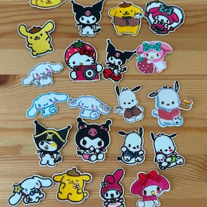 Puede incluir: Una colección de veintiún parches de tela bordados que presentan varios personajes de Sanrio, incluidos Hello Kitty, Kuromi, Cinnamoroll, Pompompurin, My Melody y Pochacco, en diversas poses, atuendos y colores como amarillo, rosa, azul y negro.