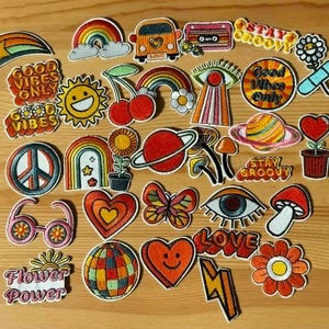 Może przedstawiać: Kolekcja kolorowych, haftowanych naszywek w stylu retro i groovy. Wzory obejmują tęcze, serca, kwiaty, znak pokoju, słońce, motyla oraz napisy "Good Vibes Only", "Stay Groovy", "Flower Power" i "Love".