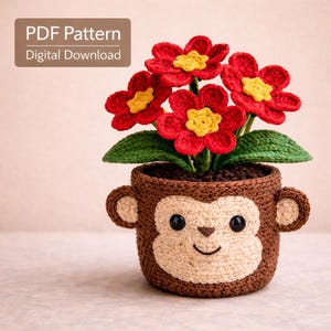 May include: A crocheted monkey-faced planter holding red and yellow flowers. The planter is brown with a light tan face, ears, and a smiling mouth. The flowers are red with yellow centers and green leaves. Text in the upper left corner reads "PDF Pattern Digital Download."