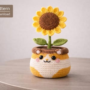 Puede incluir: Un girasol tejido a ganchillo en una maceta con una cara sonriente. El girasol tiene pétalos amarillos y un centro marrón. La maceta es de rayas blancas y amarillas con un borde marrón y orejas pequeñas. El texto a la izquierda dice "PDF Pattern Digital Download".