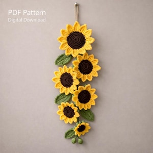 May include: A handmade crochet sunflower garland with yellow petals and brown centers, accented by green leaves. The garland is suspended from a wall. Text on the image reads "PDF Pattern Digital Download."