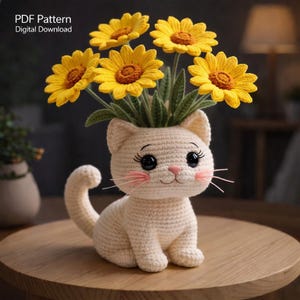 May include: A cream-colored crocheted cat-shaped planter holding yellow crocheted sunflowers. The cat has black eyes, pink cheeks, and whiskers. The text "PDF Pattern Digital Download" is in the upper left corner.