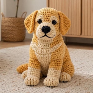 Puede incluir: Un perro golden retriever tejido a ganchillo con pecho y patas color crema. El peluche hecho a mano tiene ojos negros y nariz negra. El perro está sentado sobre una alfombra de color claro.