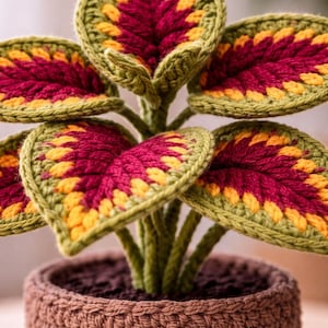 May include: A crocheted plant with green, yellow, and burgundy leaves in a brown crocheted pot. The leaves have a detailed pattern, and the pot has a textured appearance. The plant is a decorative item.