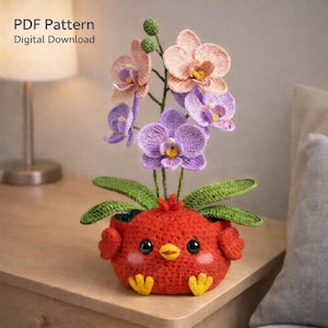Peut inclure: Un pot en forme d'oiseau rouge crocheté contenant des orchidées crochetées violettes et pêche. Le pot a des yeux noirs, un bec jaune et des pieds jaunes. Le texte "PDF Pattern Digital Download" est visible en haut à gauche.