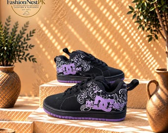 May include: A pair of black DC trainers featuring a purple logo on the side and a white floral-inspired graphic pattern. The shoes have black laces, a purple outsole, and a pull tab at the heel. The logo FashionNestPK is visible in the corner.