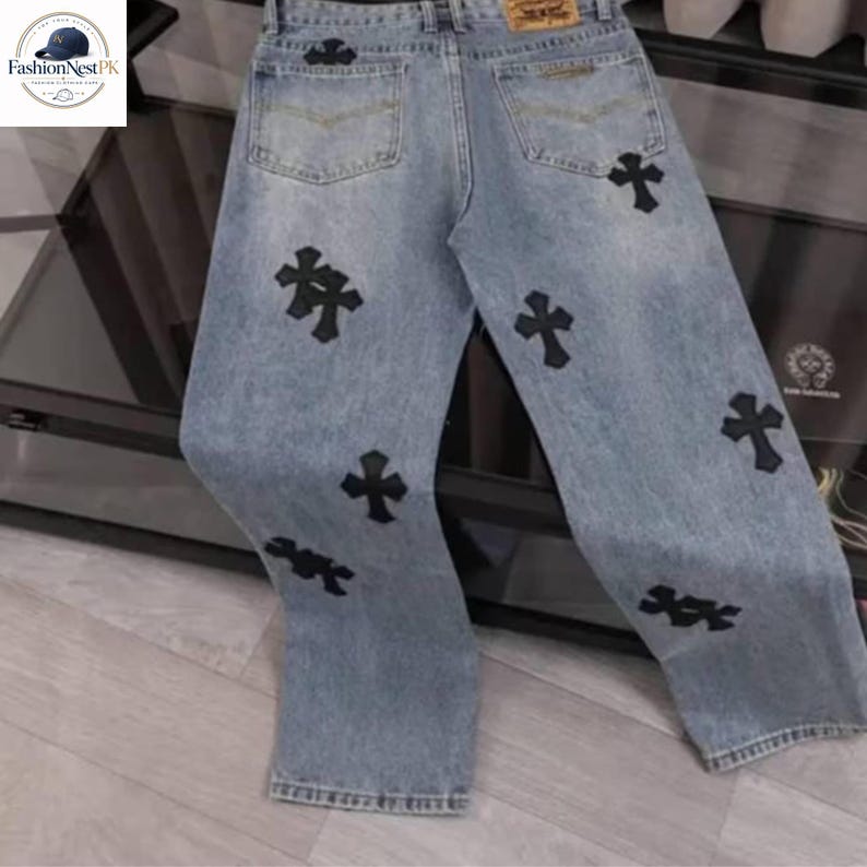 May include: Light blue denim jeans with black cross appliques. The jeans have a classic five-pocket design and a relaxed fit. The crosses are evenly spaced across the front and back of the jeans.