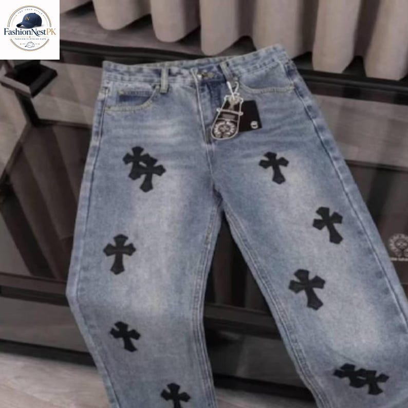 May include: Light blue denim jeans with black cross appliques. The jeans have a classic five-pocket design and a straight leg fit. A silver-tone keychain is attached to the belt loop. The jeans are a casual, everyday wear item.