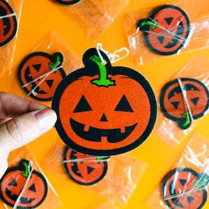 Könnte beinhalten: Orange und schwarze Kürbis-Halloween-Dekorationen mit lächelnden Gesichtern. Die Dekorationen haben grüne Stiele und sind in klarem Kunststoff verpackt. Der Hintergrund ist ein leuchtendes Orange.
