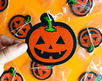 Könnte beinhalten: Orange und schwarze Kürbis-Halloween-Dekorationen mit lächelnden Gesichtern. Die Dekorationen haben grüne Stiele und sind in klarem Kunststoff verpackt. Der Hintergrund ist ein leuchtendes Orange.