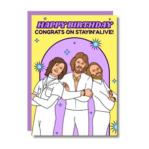 Puede incluir: Tarjeta de felicitación de cumpleaños con fondo amarillo y borde morado. La tarjeta presenta una ilustración de tres hombres con trajes blancos. El texto dice "HAPPY BIRTHDAY CONGRATS ON STAYIN'ALIVE!" con estrellas y diamantes.
