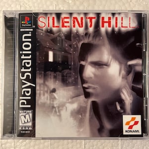 May include: A PlayStation game case for "Silent Hill." The cover art shows a grayscale portrait of a man, with the title in red. The PlayStation logo and ESRB rating are visible on the case.