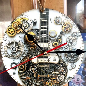 May include: Round wall clock featuring a detailed illustration of a guitar with gears and cogs. The clock face is white with black and red clock hands. The guitar design incorporates gold, silver, and black mechanical elements.