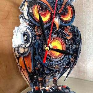 May include: A unique owl clock with a steampunk design. The clock features a detailed mechanical owl with orange, blue, and black colors. The clock hands are black with a red second hand. The owl is mounted on a clear base.
