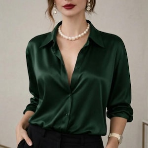 May include: A dark green satin button-down shirt with long sleeves. The shirt is paired with black pants. A pearl necklace and gold watch are visible. The shirt has a classic collar and a button-up front.