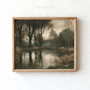 May include: A framed landscape painting featuring a calm pond surrounded by dark, silhouetted trees and tall grasses under a muted, overcast sky. The artwork is enclosed in a light-toned wooden frame, with the text VINTAGE ART PRESS printed in small, centered letters above the top edge of the frame.