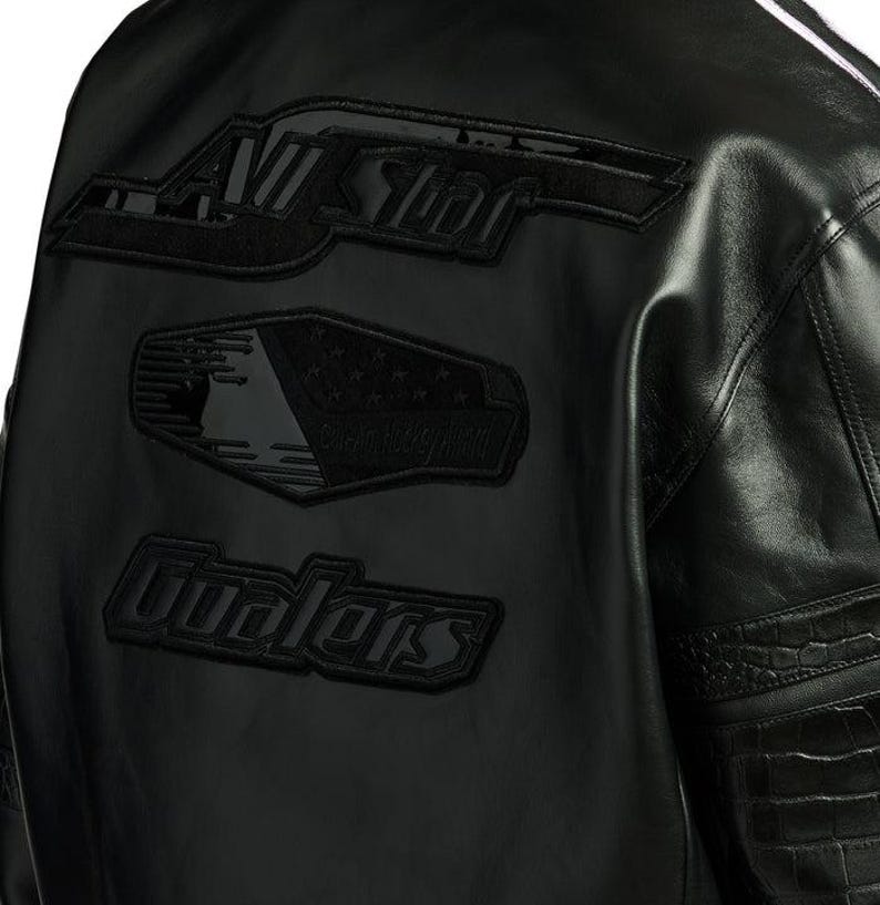 Puede incluir: Chaqueta de cuero negra con parches bordados. Los parches dicen "All Star", un dise&ntilde;o de bandera y "Gualers". La chaqueta tiene un dise&ntilde;o texturizado en las mangas y una raya blanca.