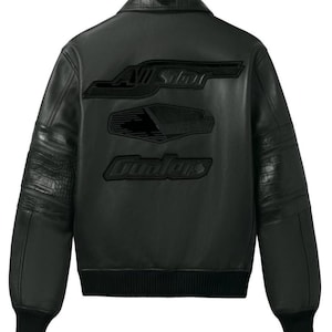 Puede incluir: Chaqueta de cuero negra con pu&ntilde;os y dobladillo acanalados. Presenta texto en relieve en la espalda que dice "All Star" y "Ovolors". La chaqueta tiene un estilo bomber cl&aacute;sico con cuello y paneles texturizados en las mangas.