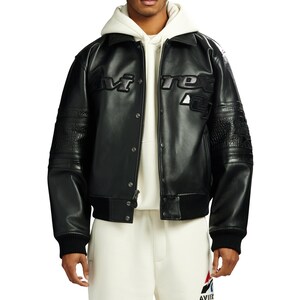 Puede incluir: Chaqueta de cuero negra con la palabra "AVIREX" en letras en relieve en el pecho. La chaqueta tiene cuello, cierre de botones y pu&ntilde;os y dobladillo acanalados. Las mangas presentan paneles texturizados. El modelo lleva una sudadera con capucha blanca debajo.
