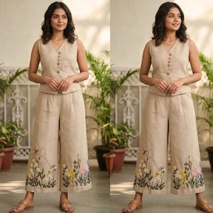 Könnte beinhalten: Beiges Leinen-Ensemble, bestehend aus einer ärmellosen Weste und einer Hose mit weitem Bein. Die Weste hat einen V-Ausschnitt und einen Knopfverschluss. Die Hose hat gestickte Blumenmuster in verschiedenen Farben am Saum. Das Outfit wird mit braunen Sandalen kombiniert.