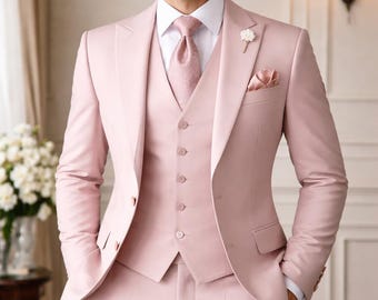 May include: A light pink three-piece suit with a matching tie and pocket square. The suit includes a blazer, vest, and trousers. A white flower pin is on the lapel. The suit is worn with a white dress shirt.