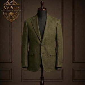 Könnte beinhalten: Ein olivgrüner Blazer auf einer Schneiderpuppe. Die maßgeschneiderte Jacke hat einen Zwei-Knopf-Verschluss, eine fallendes Revers und zwei Vordertaschen. Die Schneiderpuppe steht auf einem dunklen Holzständer vor einer braunen Wand. Das Logo "VePose - Custom Tailoring" ist sichtbar.