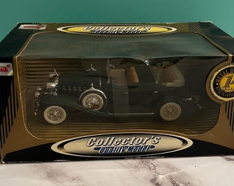 May include: A dark green die-cast metal model car with white-walled tires and a tan interior, housed in a black and gold box labeled Collector's Quality Model. The packaging features a clear plastic window and a circular gold seal on the right side.