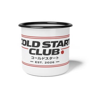 Puede incluir: Taza de esmalte blanco con borde y asa negros. La taza presenta el texto "COLD START CLUB" en letras negras en negrita, con caracteres japoneses y "EST. 2026" en negro. Dos líneas rojas rodean la taza.