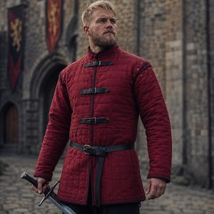 May include: A quilted, burgundy-colored medieval gambeson with black leather straps and a matching belt. The garment has a high collar and long sleeves. A sword is held in the person's hand. The background features a stone castle and banners.