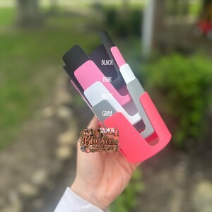 Puede incluir: Una colecci&oacute;n de fundas de tel&eacute;fono coloridas en negro, rosa, blanco, gris y salm&oacute;n. Las fundas se sostienen en una mano y est&aacute;n etiquetadas con sus respectivos colores. La marca "Bowshier Made" tambi&eacute;n es visible.