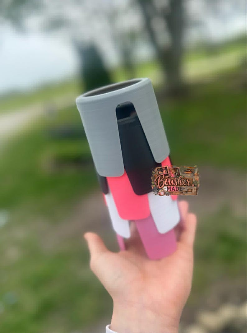 Puede incluir: Una pila de fundas de tel&eacute;fono coloridas en tonos grises, negros, rosas, blancos y magenta. Las fundas se sostienen en una mano, con el logotipo "Boushier Made" visible. Las fundas parecen ser de pl&aacute;stico.