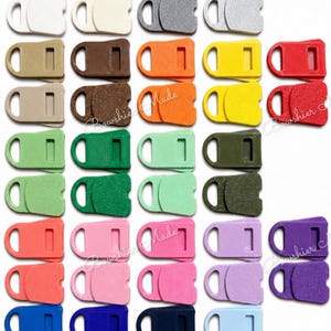 May include: A collection of colorful plastic buckle clasps in various shades, including white, gray, brown, orange, yellow, red, green, pink, purple, and blue. Each clasp features a rectangular body with a loop and a slot.
