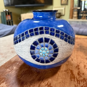 May include: A round ceramic vase with a glossy cobalt blue glaze. The centre features a textured white band decorated with a mosaic pattern of dark blue square tiles and a central circular motif composed of light and dark blue glass-like pieces.