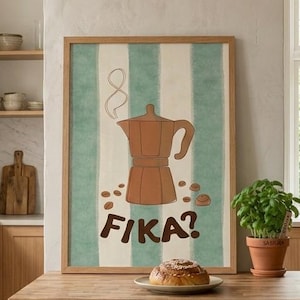 May include: A framed poster with a brown coffee maker illustration and the word "FIKA?" against a green and white striped background. A plate with a pastry sits on a wooden countertop. A potted plant is next to the plate.