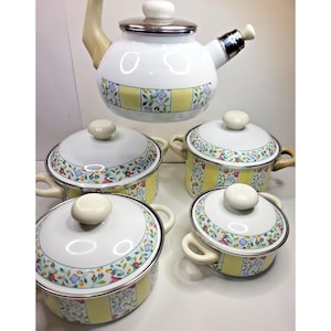 May include: A white enamel tea kettle and four matching pots with lids, each featuring a decorative pattern of yellow vertical stripes interspersed with colorful floral motifs, silver-toned rims, and cream-colored handles and knobs.