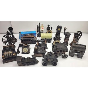 Puede incluir: Colección de sacapuntas de estilo antiguo en varias formas, incluyendo una caja registradora, teléfono, tren y escritorio. Los sacapuntas son de metal y tienen un acabado bronce o oscuro. También hay una caja azul de lápices de tranvía.