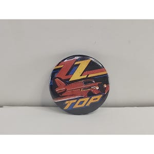 May include: A round button with a black background featuring a red car and the word "TOP" in blue and yellow. The letter "Z" is in yellow with blue accents.