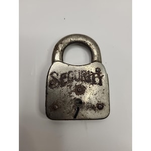 May include: A weathered, vintage padlock with the word "SECURITY" embossed on the front. The lock is made of metal and shows signs of age, with rust and wear visible on the surface. The keyhole is centered below the word.